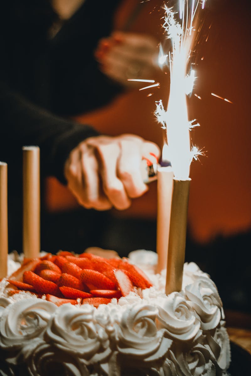 Hand lighting a sparkler candle on a strawberry cake
