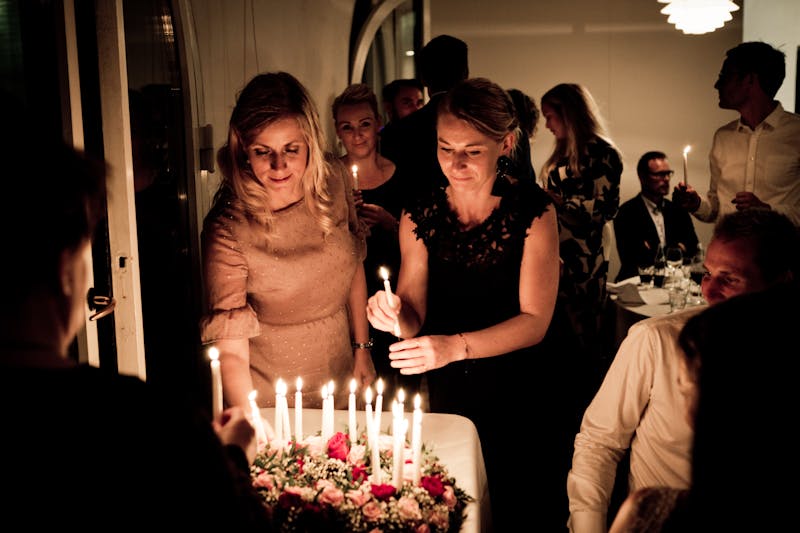 Women lighting candles on a birthday cake at a dim dinner party
